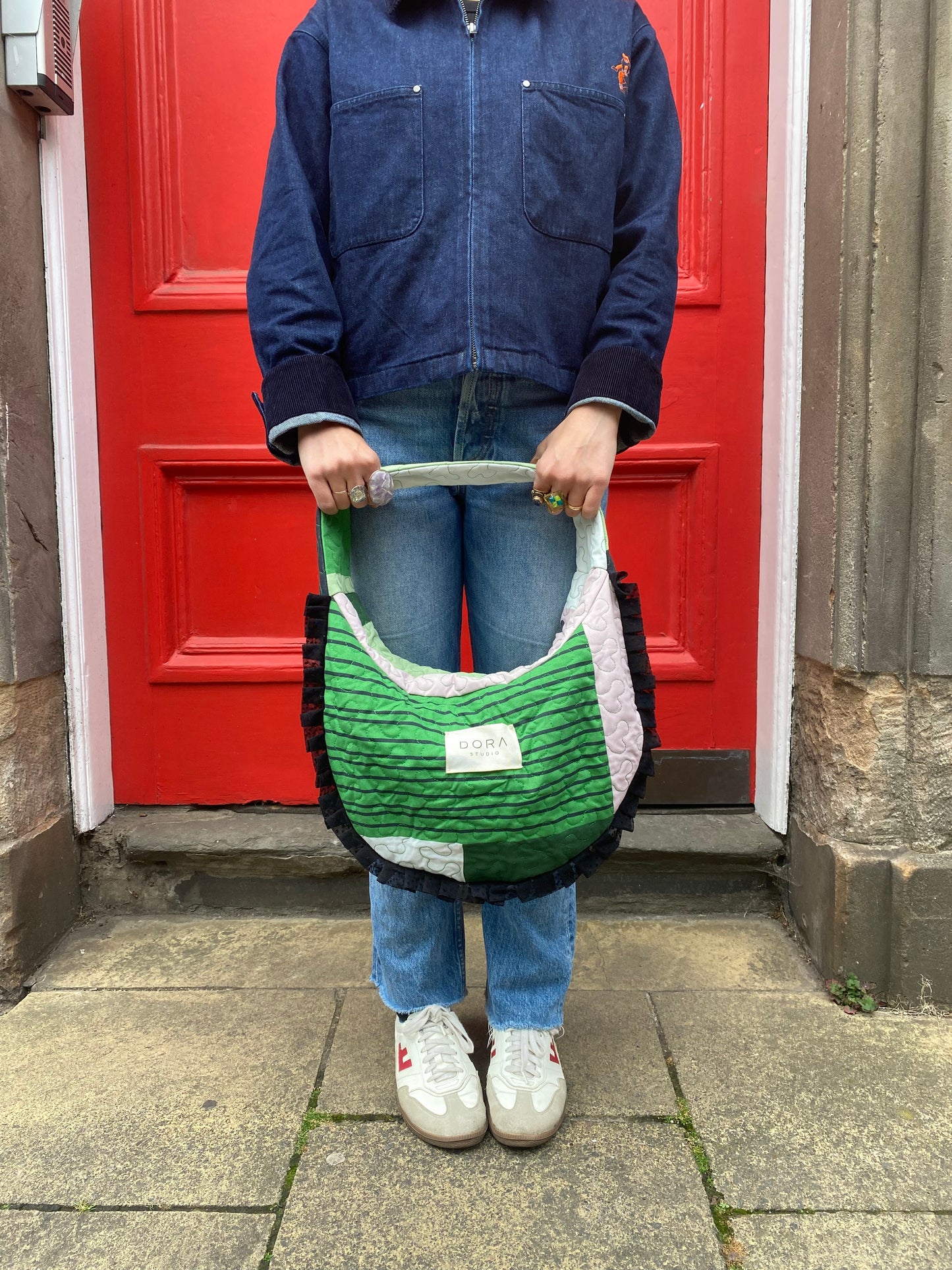 Person holding a green and black Dora Studio bag in front of a red door