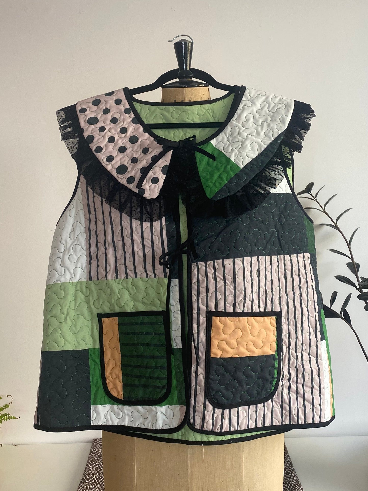 Patchwork vest on a mannequin against a white wall with plants in the background
