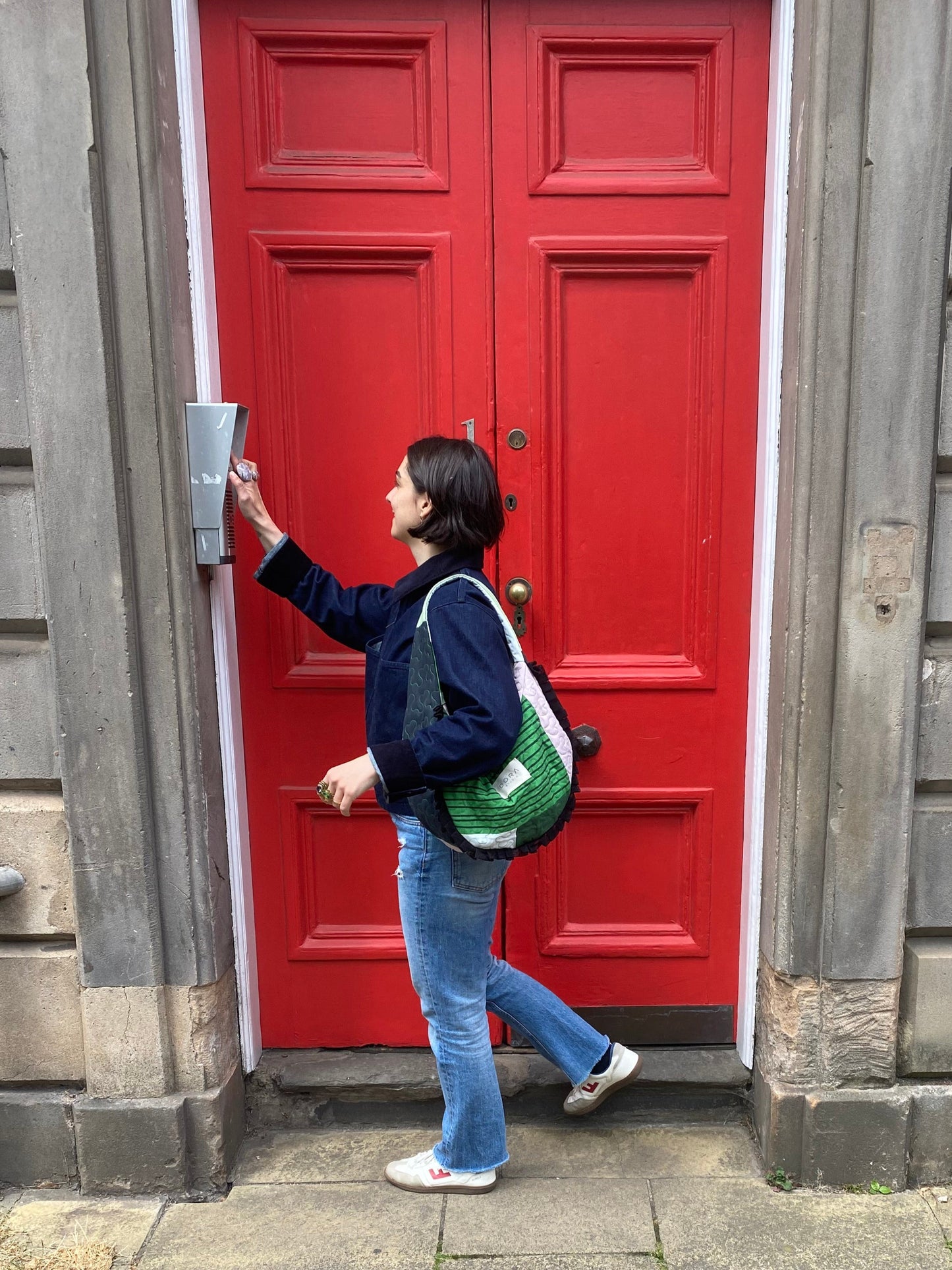 Person standing in front of a red door on a stone pavement wearing Dora Studio Frill Bag