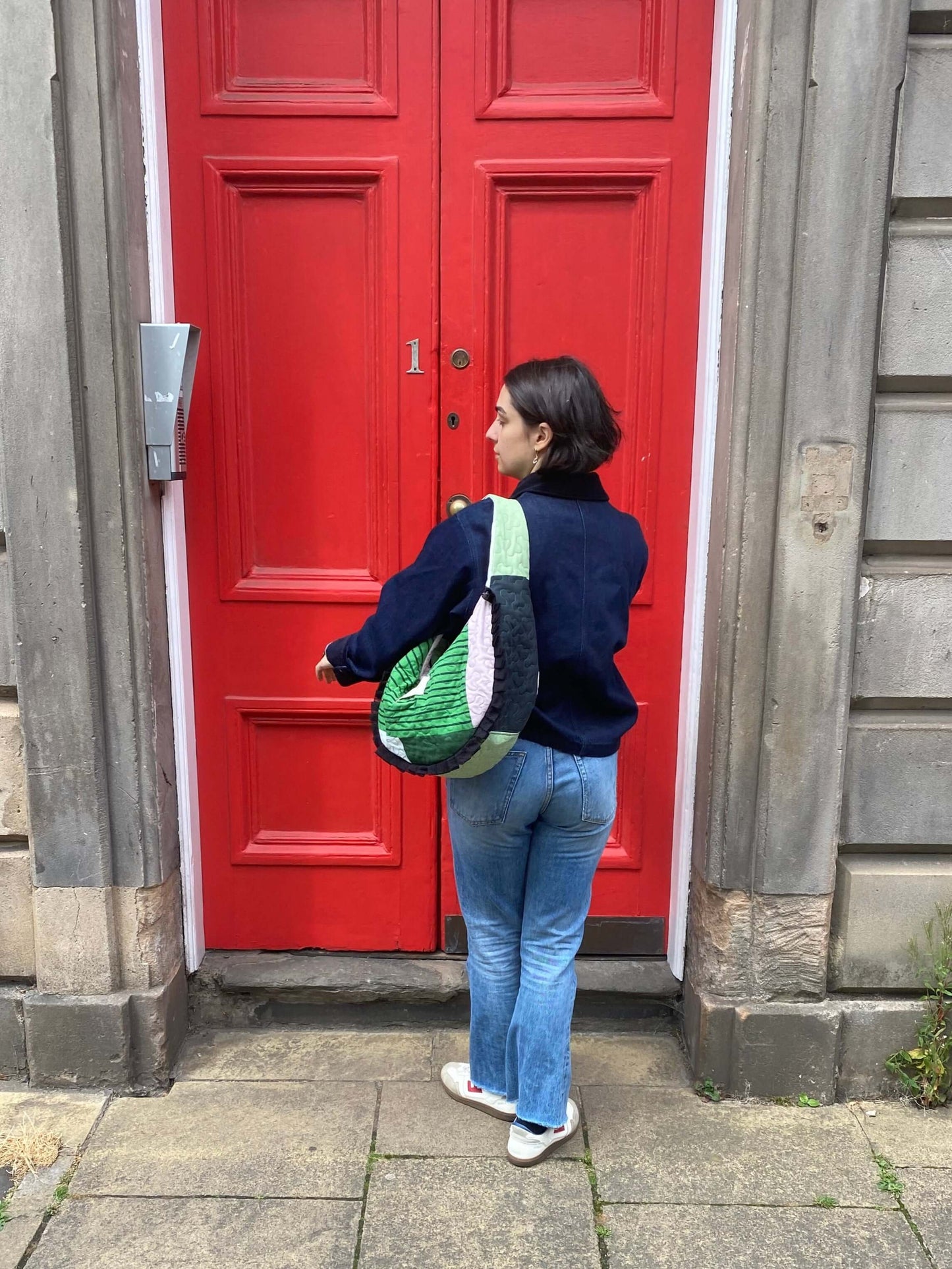 Person standing in front of a red door on a stone pavement carrying the Dora Studio Bag