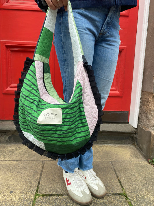 Person holding a green and white patterned bag with a visible brand logo in front of a red door.
