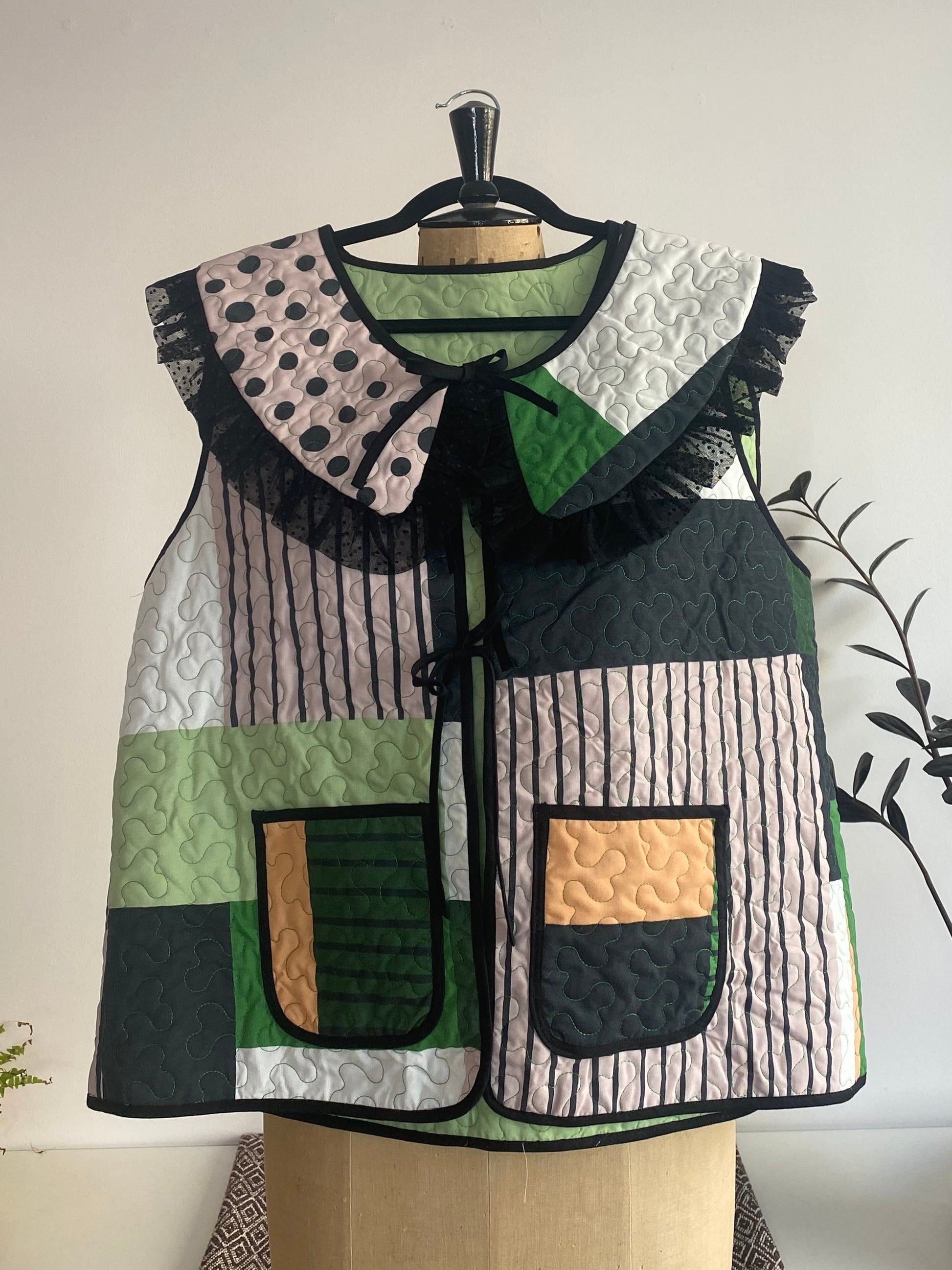 Patchwork vest on a mannequin against a white wall with plants in the background
