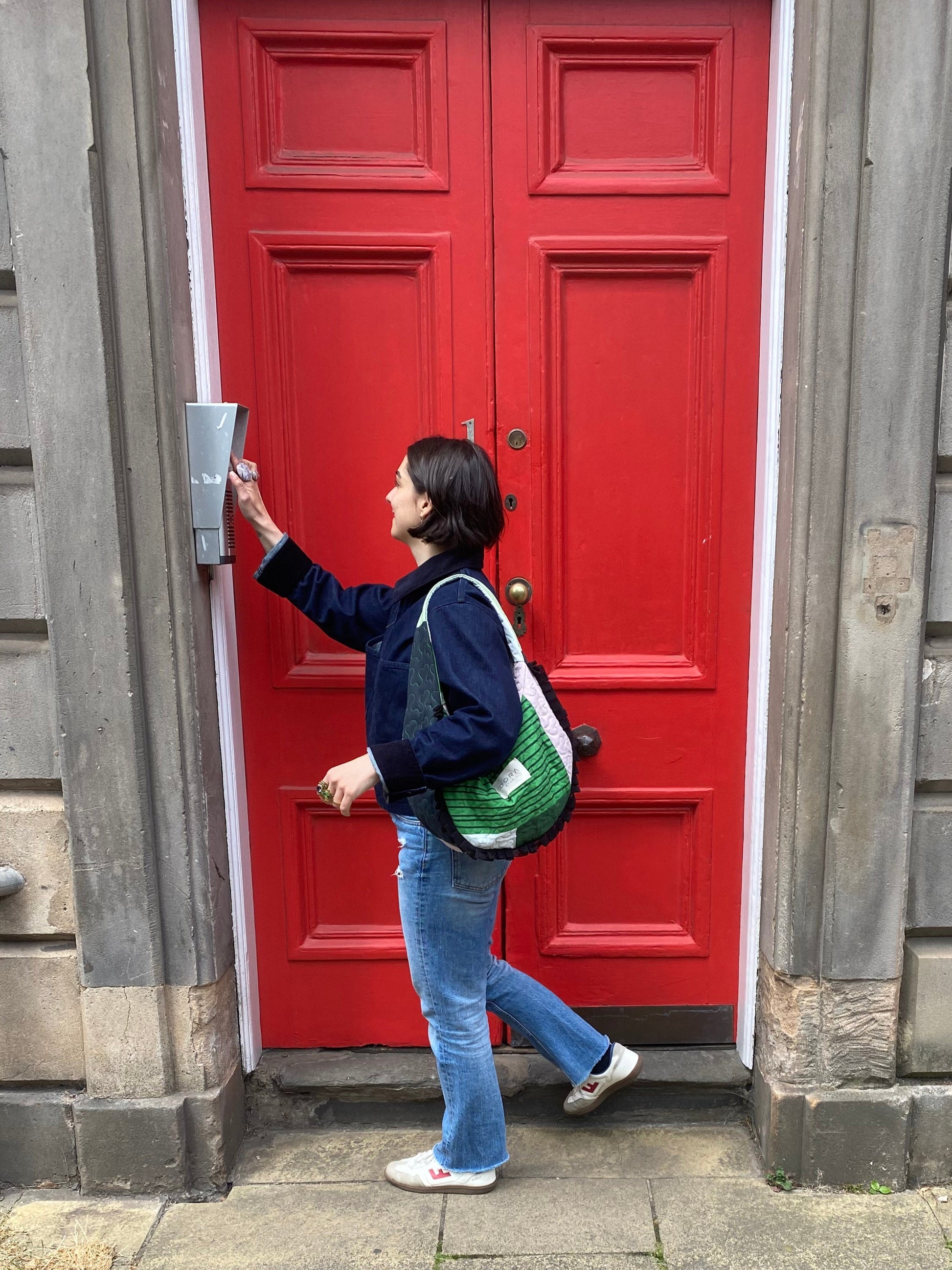Person standing in front of a red door on a stone pavement wearing Dora Studio Frill Bag