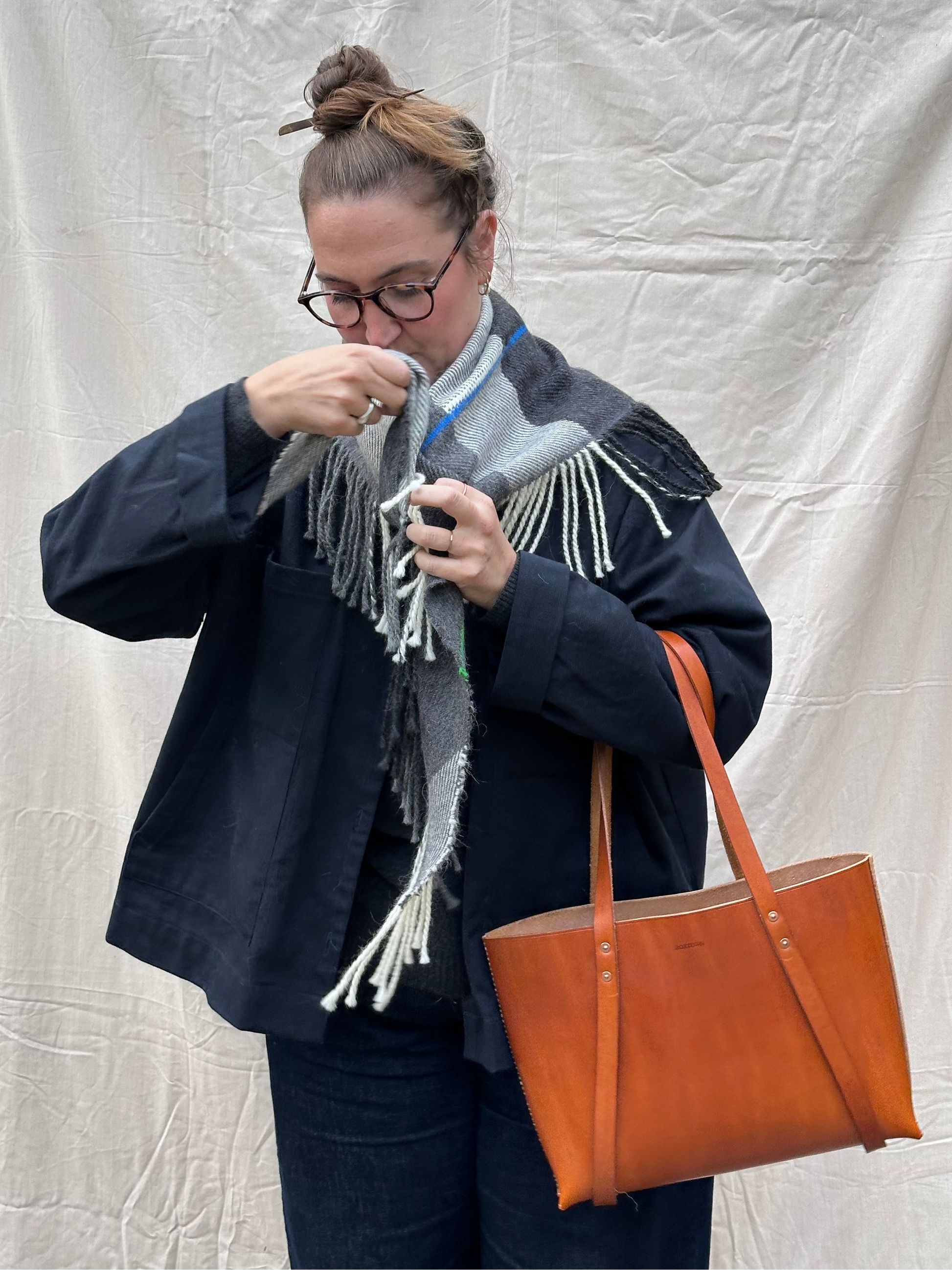 Woman adjusting a scarf with a brown leather tote bag against a white backdrop