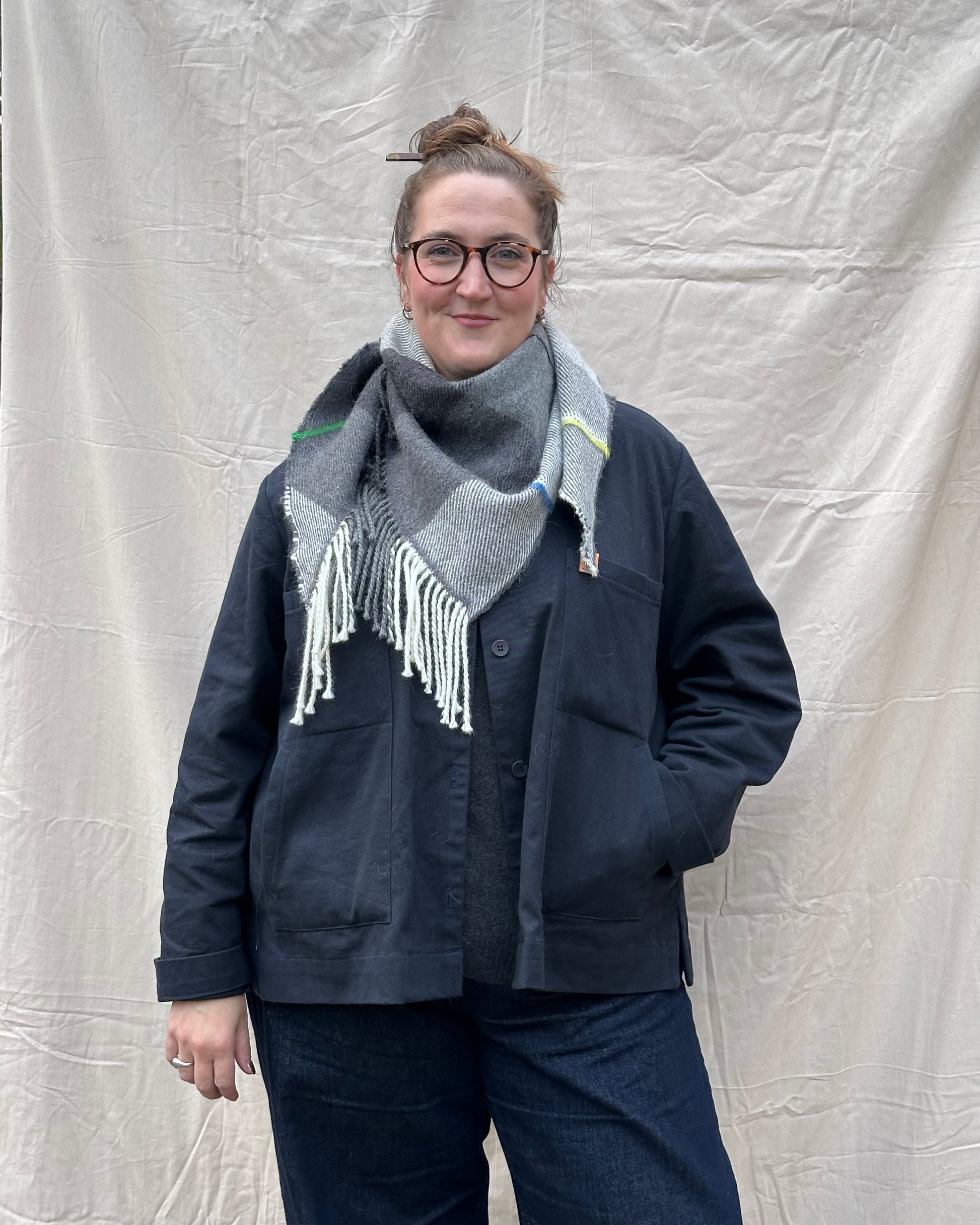 Person wearing a dark jacket and gray scarf against a plain background