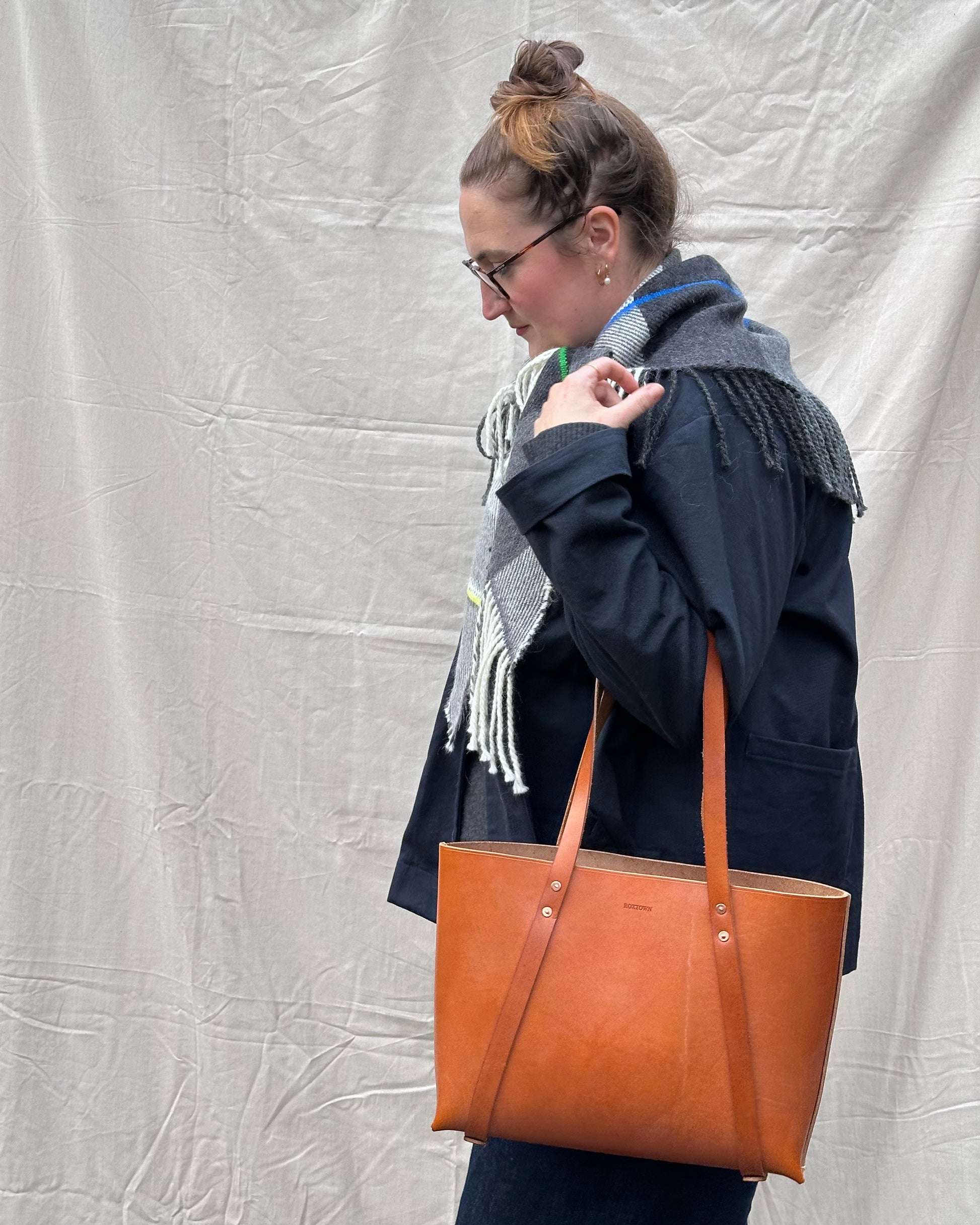 Woman holding a brown leather tote bag against a plain background