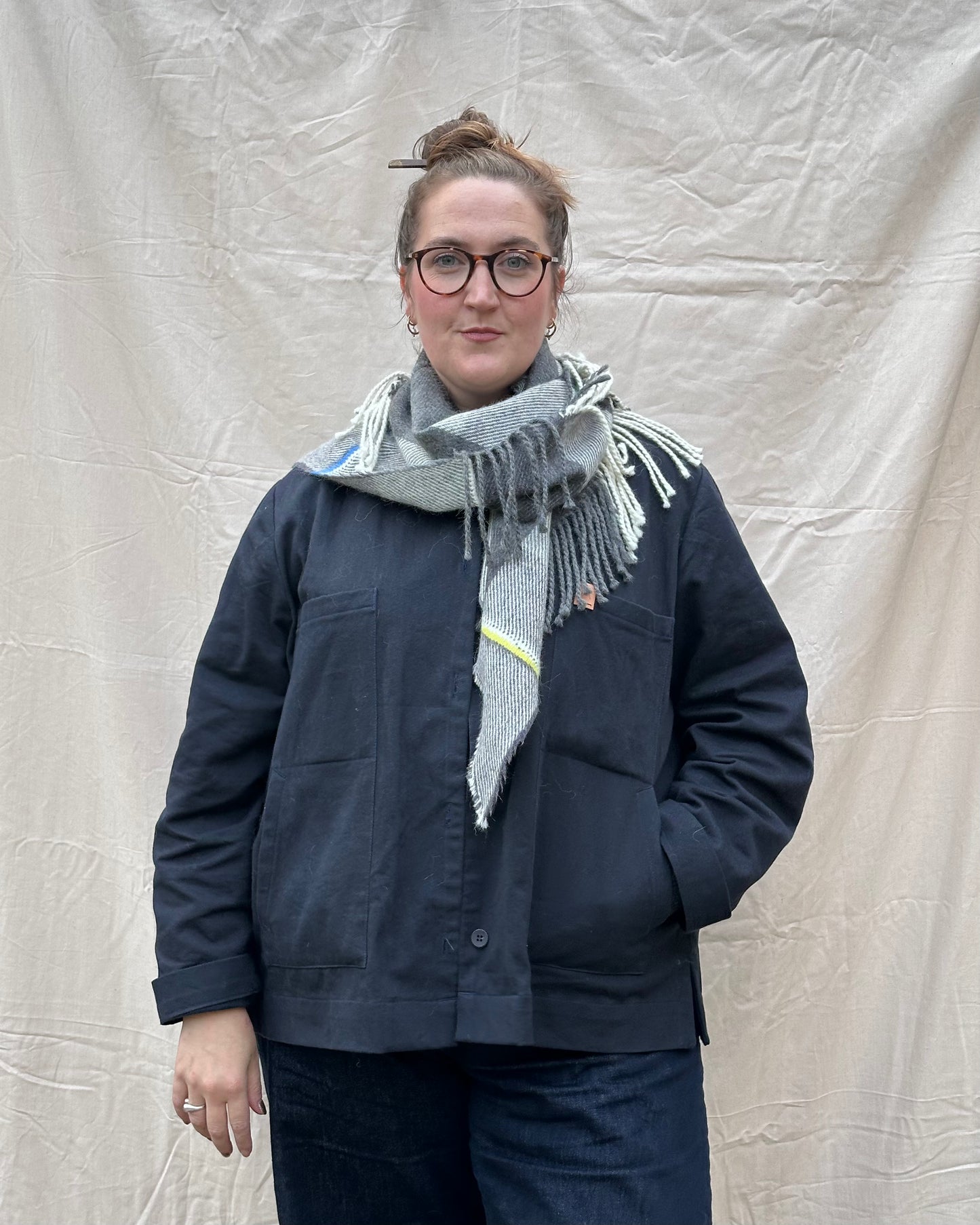 Person wearing a navy jacket and gray scarf against a plain background