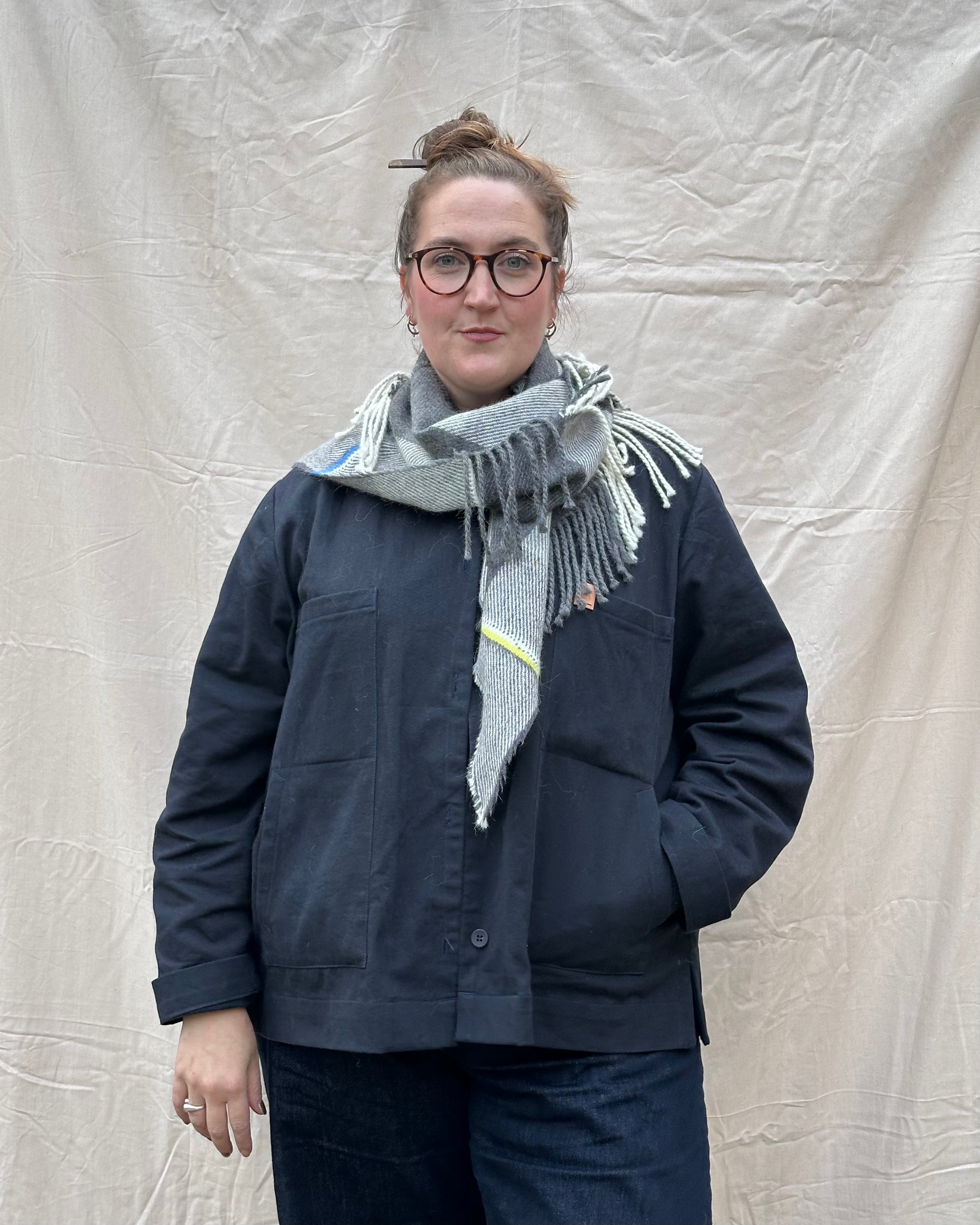 Person wearing a navy jacket and gray scarf against a plain background