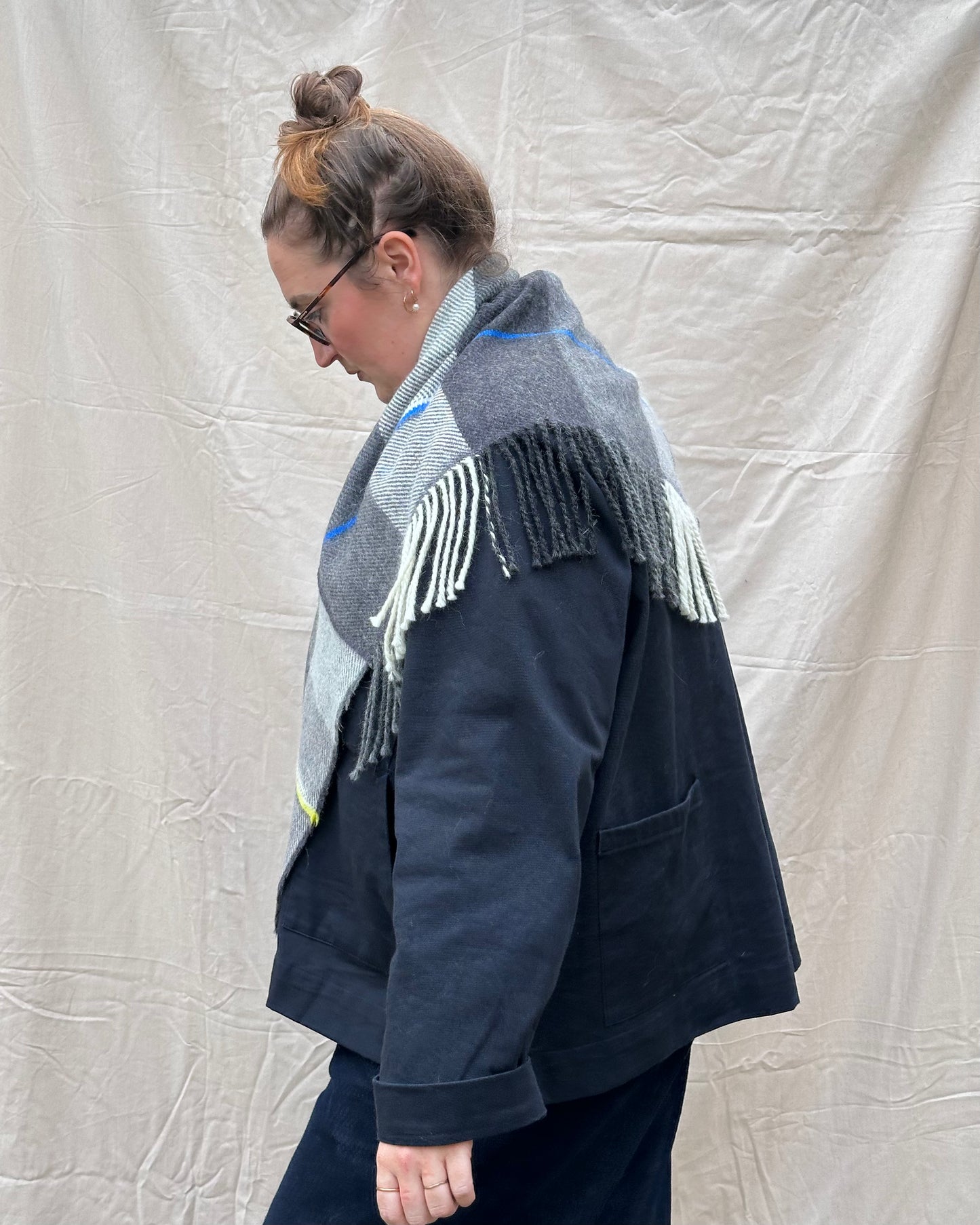 Person wearing a dark blue jacket and a patterned scarf against a plain background