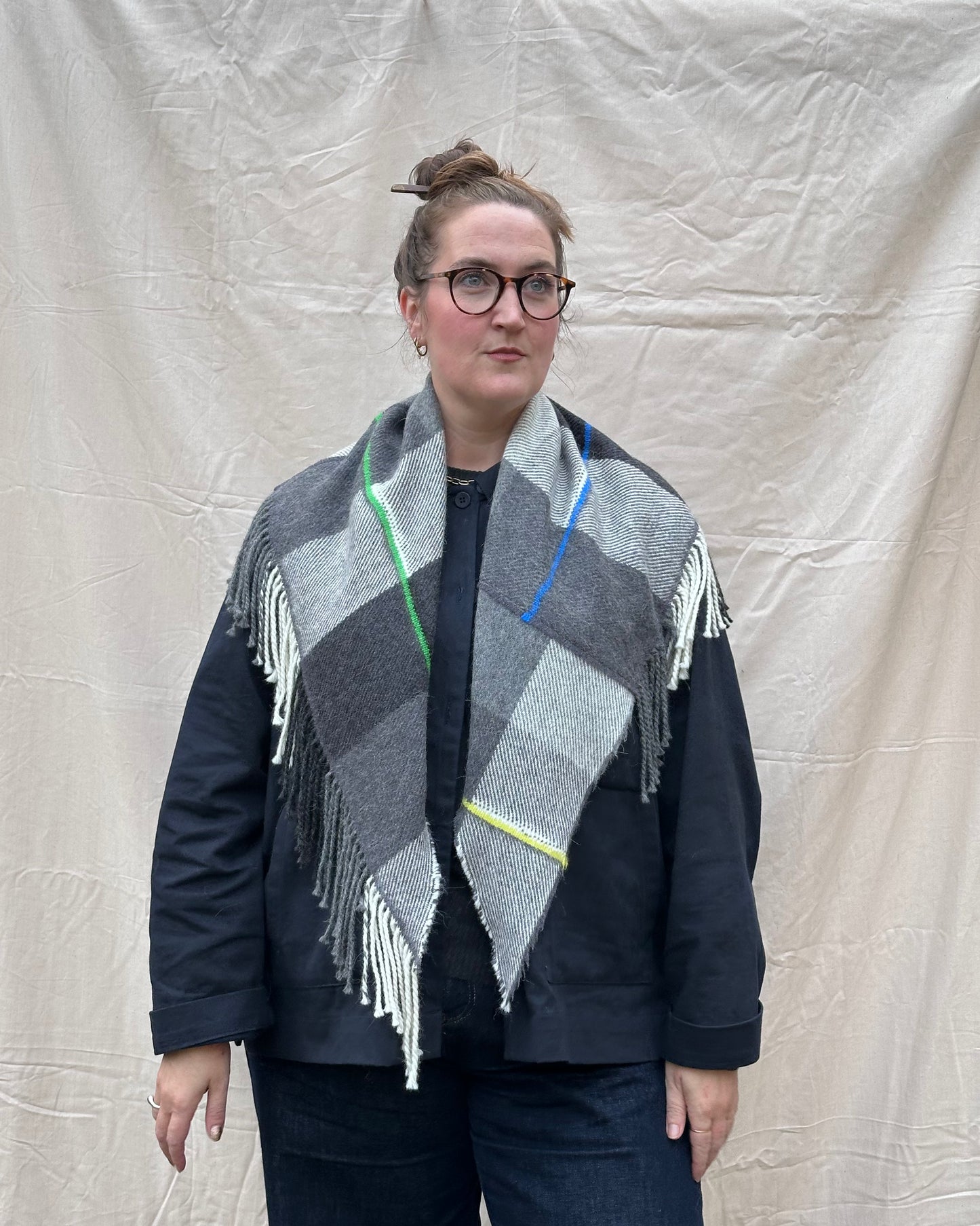 Person wearing a patterned scarf with fringes against a plain background